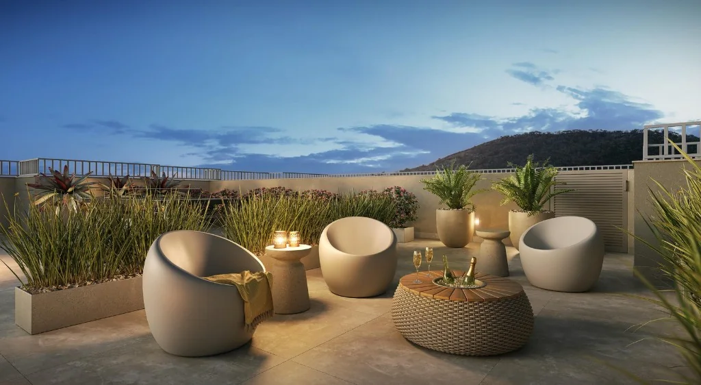 Terraço ao entardecer com poltronas, mesa central e iluminação ambiente.